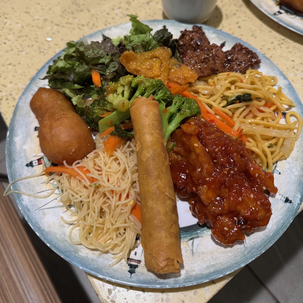 A big plate from Grasshopper's vegan Sunday buffet: salad greens, broccoli, a spring roll, rice noodles, lo mein, slices of mock beef, a fried dumpling, and a sticky sesame-glazed dish.