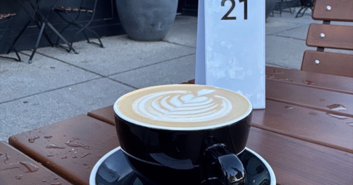 A Tahini Pumpkin Oatmilk Latte at Tatte, with rosetta latte art, on a patio table.