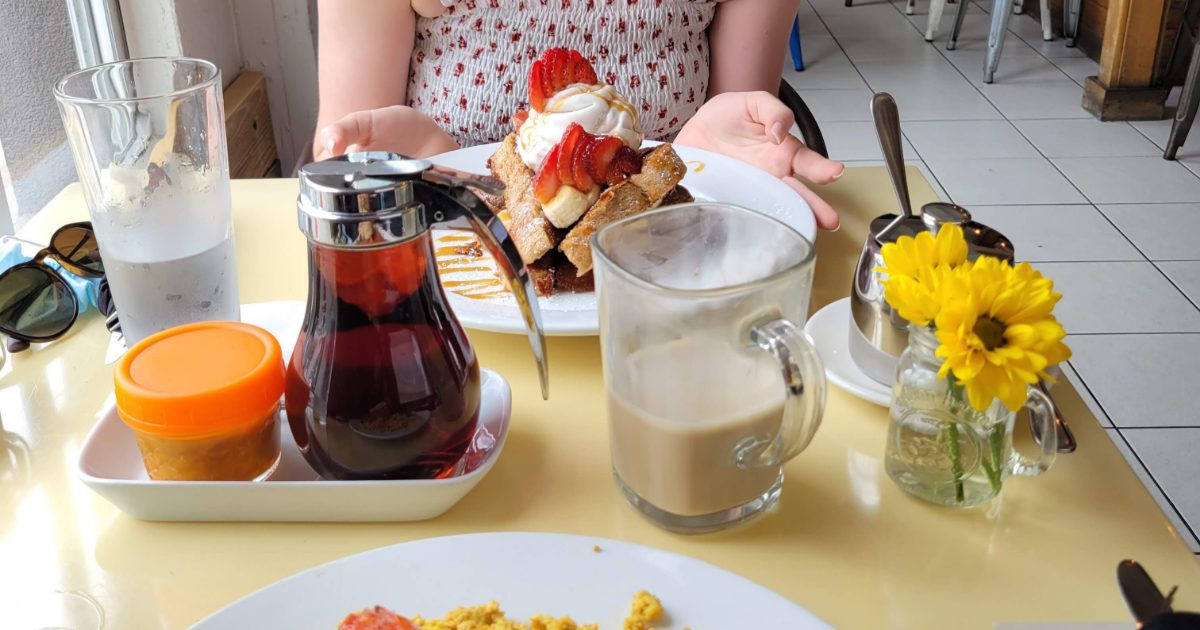 A vegan brunch table: French toast with strawberries, maple syrup, an oat milk latte, and a tofu scramble plate.